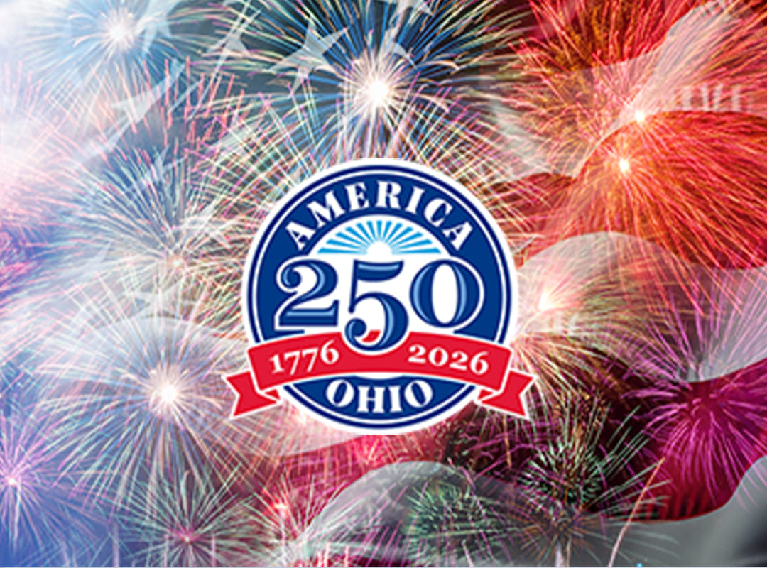 Fireworks bursting over an American flag with an America 250 Ohio emblem, representing a twilight air show and pyrotechnic celebration honoring 250 years of American independence.
